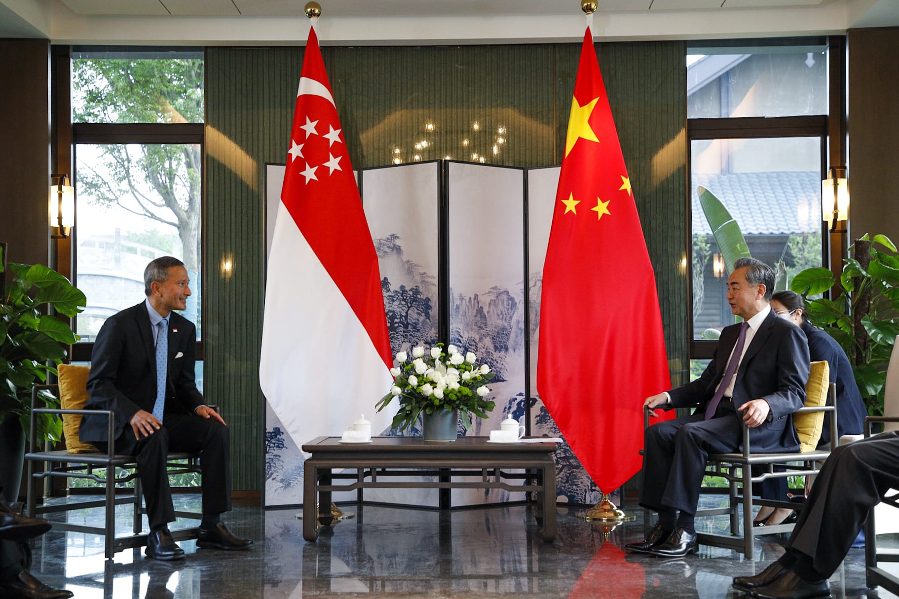 Two men in suits seated, Singapore and China flags in background.